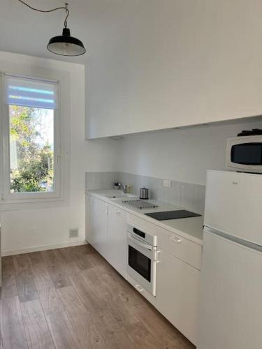 une cuisine blanche avec une cuisinière et une fenêtre dans l'établissement La maison de Camille climatisation parking privé WIFI, à Carcassonne
