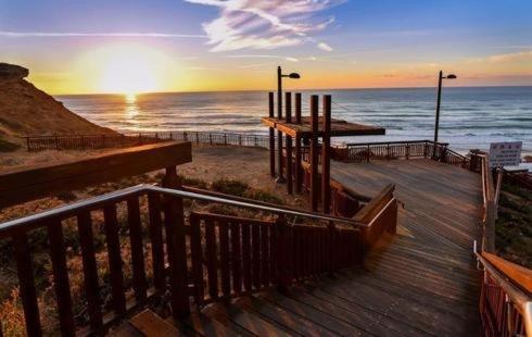 a sunset over the ocean with a wooden boardwalk at the pool on the sea in Netanya