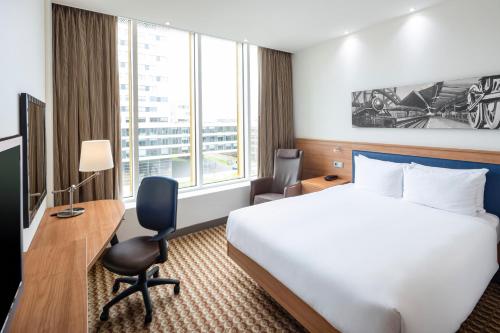 a hotel room with a bed and a desk and a large window at Hampton by Hilton Amsterdam Airport Schiphol in Hoofddorp