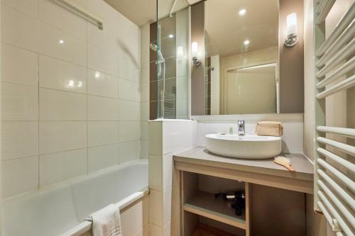 a bathroom with a sink and a tub and a mirror at Pierre & Vacances Résidence Le Chant des Oiseaux in Courseulles-sur-Mer