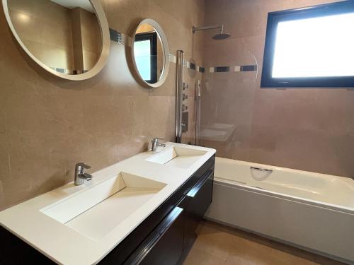 y baño con 2 lavabos, espejo y bañera. en Villa de lujo con vistas al mar y piscina privada, en Santa Susanna