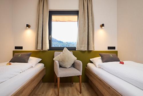 two beds in a room with a chair and a window at Siplinger Suites - Ferienwohnungen und Suiten - Sauna und Fitness in Balderschwang