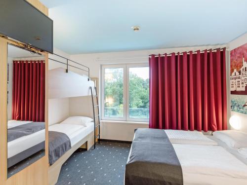 a bedroom with two beds and a window with red curtains at B&B Hotel Lüneburg in Lüneburg