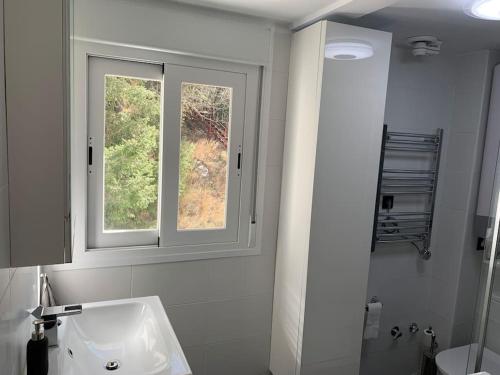 La salle de bains blanche est pourvue d'un lavabo et d'une fenêtre. dans l'établissement APARTAMENTO PRECIOSO SOL Y SIERRA, à Sierra Nevada