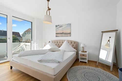a white bedroom with a bed and a large window at ANYTIME - Riedlepark Apartments in Friedrichshafen