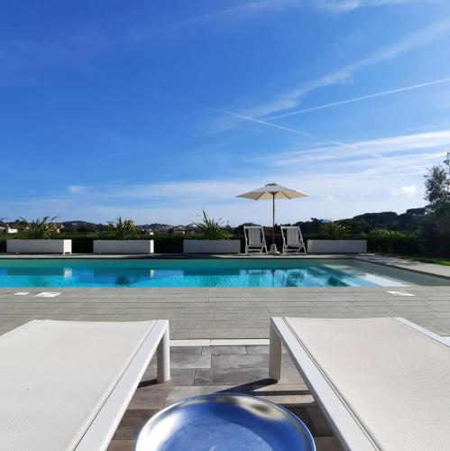 ポルトフェッラーイオにあるLa Suite con Piscina Privataの白いベンチ2台とパラソル付きのスイミングプール