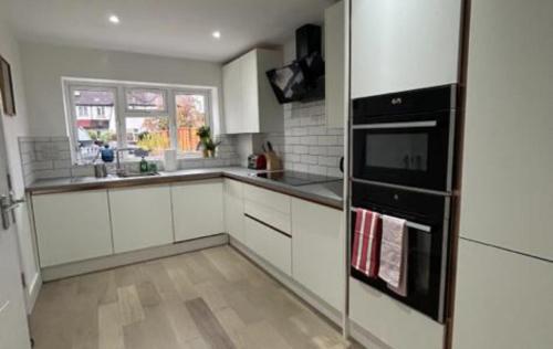 a kitchen with white cabinets and a black refrigerator at London Stunning Three Bedroom House in Mitcham