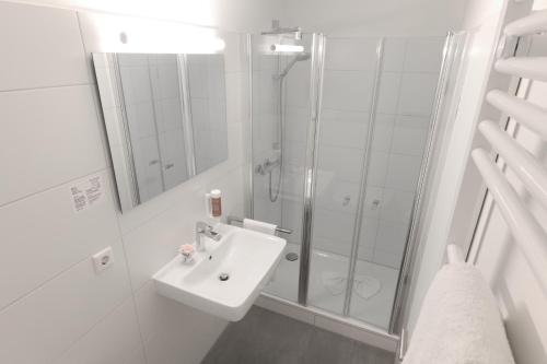 a white bathroom with a shower and a sink at Hotel Kühl in Neumünster