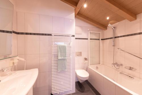a white bathroom with a toilet and a tub and a sink at Quality Hosts Arlberg - Hotel Bergheim in Sankt Anton am Arlberg