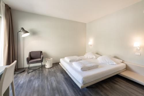 a white bedroom with a bed and a chair at Hotel Baia Azzurra - Lake Front in Nago-Torbole