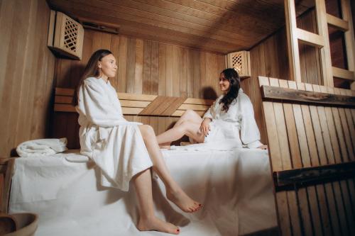 two women sitting on a bed in a sauna at Vila Poiana Vadului in Vadul lui Vodă