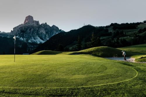 a person standing on a golf course with a mountain in the background at Pensione Haus Erica in Colfosco