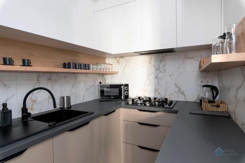 a kitchen with white cabinets and a black counter top at Baltic Breeze Apartment 3city Gdańsk by Noclegi Renters in Gdańsk