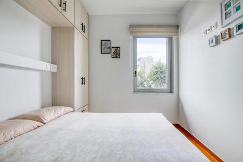 a white bedroom with a bed and a window at Athena's South Apartment in Athens