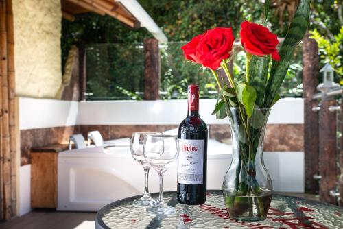 Una botella de vino y dos vasos y un jarrón con rosas. en Finca Ecológica El Maco, en San Agustín