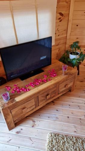 uma grande televisão de ecrã plano numa mesa de madeira com flores em The Cabin at Ashleigh House em Gaerwen