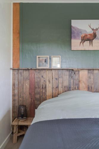 a bed with a wooden headboard with a deer on the wall at Wildzicht Cosy Cabins in 't Zand
