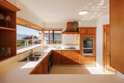 a kitchen with wooden cabinets and a large window at Absolute Beachfront Holiday Home With Private Beach Access To Swim Beach Spectacular Sunsets in Paraparaumu