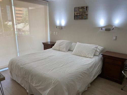 1 dormitorio con 1 cama con sábanas blancas y 2 mesas en Kennedy Premium Apartments Colorado, en Santiago