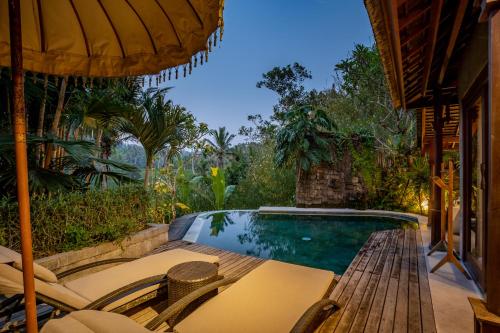 a swimming pool with chairs and an umbrella at Nau Villa Ubud in Tegalalang