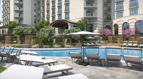 uma piscina do hotel com mesas e cadeiras e um guarda-sol em The Ritz-Carlton Dallas, Las Colinas em Irving