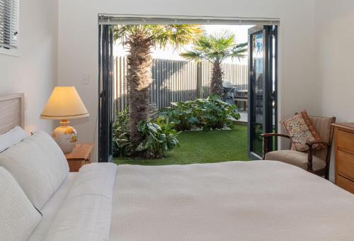 a bedroom with a bed and a patio with palm trees at The Ocean Outlook Pure Luxury in New Plymouth