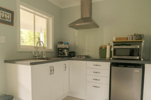 a kitchen with white cabinets and a sink and a microwave at Birdsong Cottage in Paraparaumu