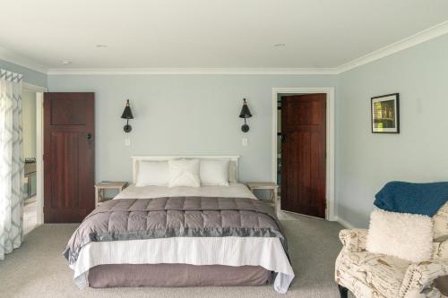 a bedroom with a large bed and a chair at Birdsong Cottage in Paraparaumu