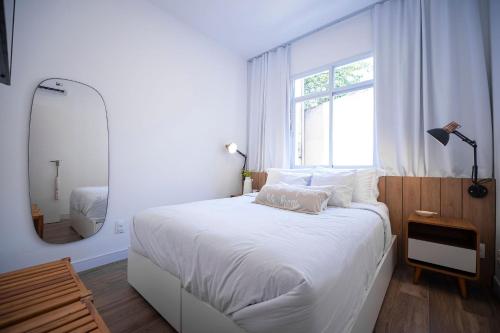 ein weißes Schlafzimmer mit einem großen Bett und einem Spiegel in der Unterkunft Conforto e praticidade na Gávea -por Casapē in Rio de Janeiro
