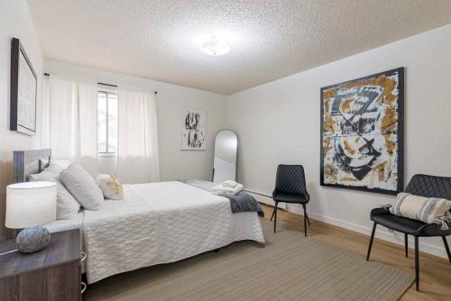 a bedroom with a white bed and two chairs at COZY 1BR Top Floor with Balcony Newly Renovated in Fort McMurray