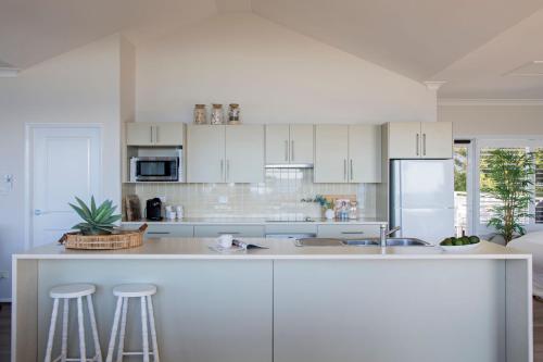 a kitchen with white cabinets and a counter with stools at Kalinda in Mollymook