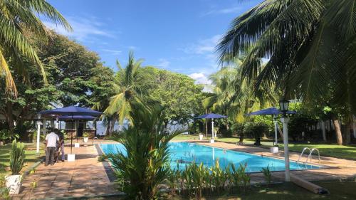 un hombre de pie junto a una piscina con sombrillas azules en Hotel Lagoon Paradise, en Negombo