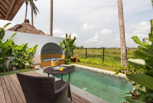 a patio with a table and chairs next to a swimming pool at Suga Estate - Rice Field View Villas in Ubud