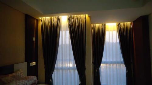 a bedroom with two large windows with curtains at Apartemen Skylounge Makassar in Manda