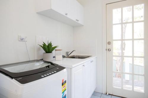a white kitchen with a sink and a dishwasher at The Treehouse Vincentia in Vincentia