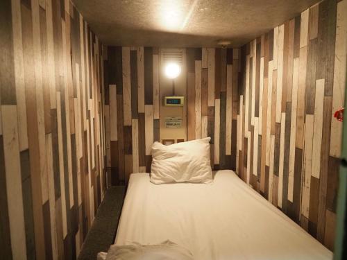 a bed with a pillow in a room with wooden walls at Capsule Hotel Block Room in Tokyo