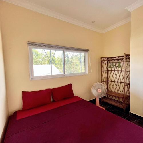 a bedroom with a red bed and a window at CornerStone Nesat in Nesat Village in Phumĭ Chroŭy Svay