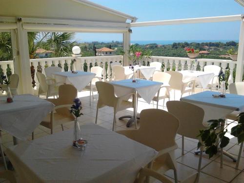 um restaurante com mesas brancas e cadeiras numa varanda em Ionion Star Hotel em Tholón