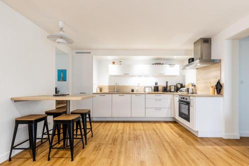 une cuisine avec des armoires blanches et des tabourets de bar dans l'établissement L’Auguste - Appartement Terrasse, 450m de la plage, à Royan