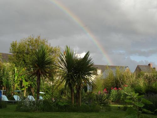 a rainbow in the sky over a garden with palm trees at Gîte "ROSE des SABLES" - PISCINE jusqu'au 15 SEPTEMBRE, JARDIN BOTANIQUE, COMMERCES &MER in Surtainville