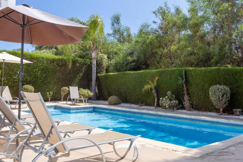 a swimming pool with chairs and an umbrella at Villa Shanta in Peyia