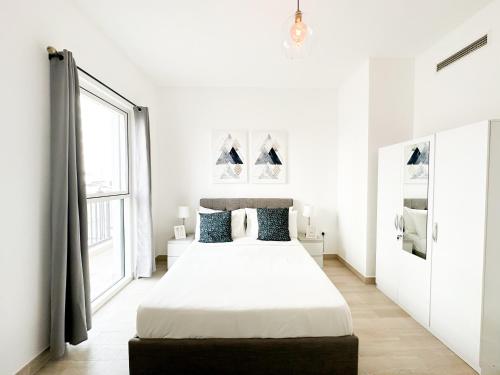 a white bedroom with a large bed and a window at Cozy Chic Corner G04WB3 in Abu Dhabi
