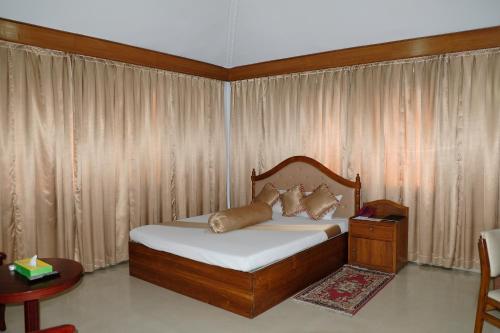 Hotel Saint Martin Ltd. في شيتاغونغ: غرفة نوم بسرير مع اطار خشبي وستائر