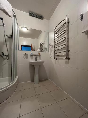 La salle de bains blanche est pourvue d'un lavabo et d'une douche. dans l'établissement Hotel - cafe Naujoji Akmenė, à Naujoji Akmenė