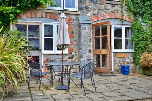 a table and chairs with an umbrella on a patio at Finest Retreats - Little Dunley - Wisteria Cottage in Bovey Tracey