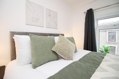 a bed with green and white pillows and a window at K Suites - Seymour Street in Mountain Ash