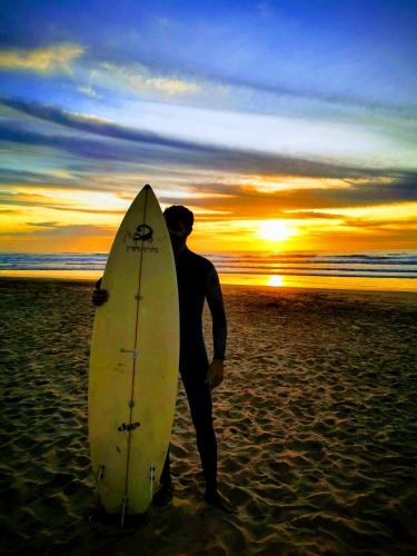 a man standing on the beach with a surfboard at Hill Valley Asilah - Luxury Living & Boutique Hotel in Asilah