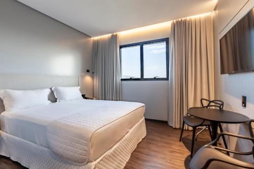 Tri Hotel Premium Itapema في ايتابيما: غرفة فندقية بسرير كبير وطاولة