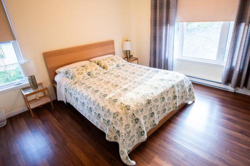 a bedroom with a bed with a floral bedspread and two windows at L'Évasion in Lambton