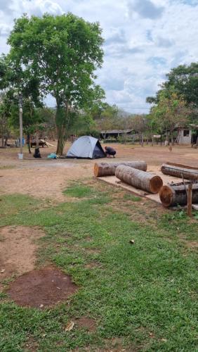 a tent and some logs in a field with a tree at pousada camping do josias in Nobres